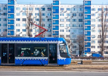 Kyiv, Ukrayna - Mart 2025: Geleneksel desenlerle süslenmiş mavi bir tramvay konut binalarının önünden geçiyor. Yolcular yolculuklarının tadını çıkarırken günlük hayat etraflarında enerji dolu olarak dolaşıyor..