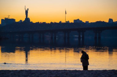 Kyiv, Ukrayna - 20 Mart 2025: Dnipro nehrinin kumsalında dinlenen insanlar, Ukrayna 'nın mücadelesinin sembolü olan Ukrayna' nın Ukrayna 'daki tam ölçekli Rus işgalinin (24 Şubat 2022) ve Nat' ın bir parçası olan Ukrayna Anıtının manzaralı manzarasına karşı
