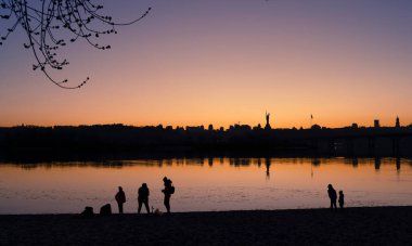 Kyiv, Ukrayna - 20 Mart 2025: Dnipro nehrinin kumsalında dinlenen insanlar, Ukrayna 'nın mücadelesinin sembolü olan Ukrayna' nın Ukrayna 'daki tam ölçekli Rus işgalinin (24 Şubat 2022) ve Nat' ın bir parçası olan Ukrayna Anıtının manzaralı manzarasına karşı