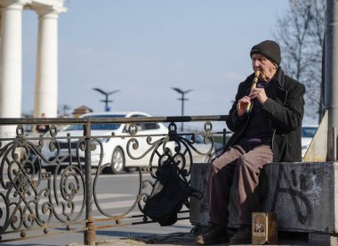Kyiv, Ukrayna - 1 Nisan 2025: Yaşlı bir müzisyen, Kyiv 'deki günlük yaşamın telaş ve telaşıyla çevrili bir şehir caddesinde flüt çalıyor. poshtova karesi