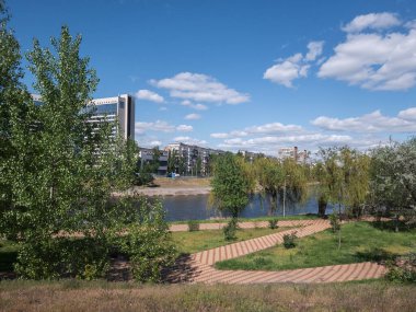 Rusanivka yerleşim bölgesi, Dnipro kanalı boyunca açık mavi gökyüzü ve dağınık bulutların altında yeşil alanlar ve modern binaların bir karışımını sergiliyor..