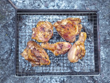 Tavuk budu ve baldırları kızgın kömür közlerinde ızgara yapıyor, açık havada yemek pişiriyor.