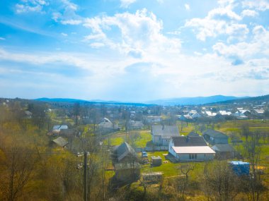 Küçük köy evleri, yeşil çayırlar, tepeler ve bulutlu mavi gökyüzünün altındaki dağlar ile Ukrayna kırsalının güzel bahar panoramik manzarası.