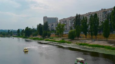 Dnipro nehrinin kıyısındaki konut binaları, pedallı teknelerin sakin bir şekilde sularda yüzdüğü, şehrin manzarasını sunan,