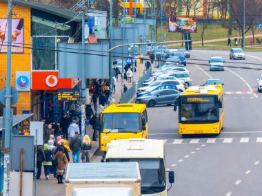 Kyiv, Ukrayna - 20 Mart 2025: Bulutlu bir günde Riga, Letonya 'daki otobüs durağında Vodafone ve diğer dükkanlarla birlikte sarı toplu taşıma otobüsleri sürüp duruyor