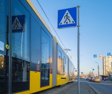 Kyiv, Ukrayna -6 Mart 2025: Ukrayna 'da açık mavi bir gökyüzünün altındaki kentsel manzarayı yansıtan yaya geçidi işaretinin yanına park edilmiş sarı tramvay