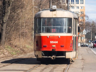 Kyiv, Ukrayna -6 Mart 2025: Güneşli bir günde Ukrayna 'da bir konut binası ve çıplak ağaçların yanında 15 numaralı eski kırmızı ve bej tramvay raylardan geçiyor
