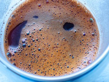 Taze demlenmiş kahve bir cam bardağı doldurur, köpüğü karmaşık bir köpük ve koyu sıvı deseni oluşturur, bu popüler içeceğin büyüleyici yakın çekimini sunar.