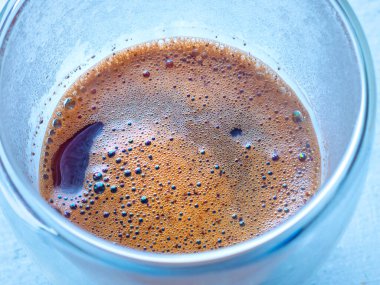 Şeffaf cam bardakta köpüklü taze demlenmiş kahve güzel bir kalıp oluşturuyor, mükemmel bir sabah içeceğinin özünü yakalıyor.