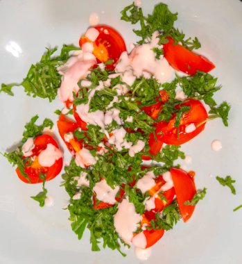 Dilimlenmiş domates ve krema soslu taze roka açık mavi bir tabakta servis edilir. Basit ama iştah açıcı sağlıklı bir yemek oluşturur.