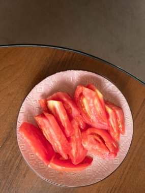 Bir kaç sulu domates dilimi, ahşap bir masanın üzerinde duran dekoratif pembe bir tabakta, canlı ve iştah açıcı bir sahne yaratıyor.