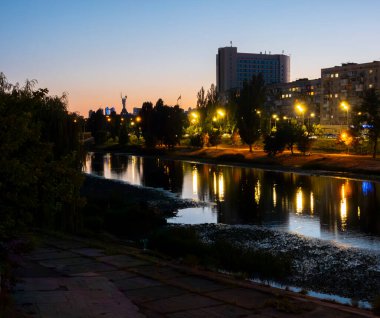 Dnipro Nehri, Ukrayna 'nın başkenti Kyiv' de bulunan Ukrayna Anıtı ve renkli gökyüzü ile binalardan ve sokak lambalarından alacakaranlıkta yapay ışıkları yansıtıyor.