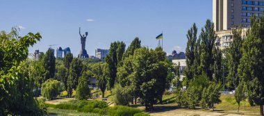 Bereketli yeşil ağaçlar ve Dinyeper nehir kanalı Ukrayna 'nın ulusal kimliğinin sembolü olan ikonik Ana Ukrayna Anıtı' nı modern binaların ve Kyiv 'de berrak mavi bir gökyüzünün zeminine karşı çerçeveler.