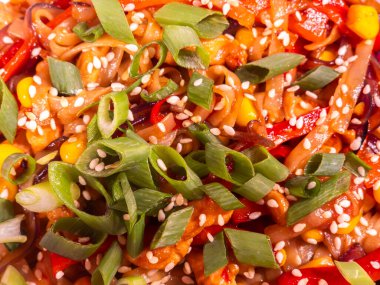 Tavukla, mısırla, biberle ve taze soğanla kızartılmış Udon erişteleri, susam tohumlarıyla süslenmiş, canlı ve lezzetli bir Asya yemeği yaratıyor.