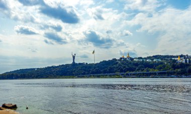 Ana Ukrayna Anıtı ve Kyiv Pechersk Lavra 'nın (Mağaraların Kiev Manastırı) ön planda Dnipro nehri ile bulutlu bir gökyüzünün altında manzarası