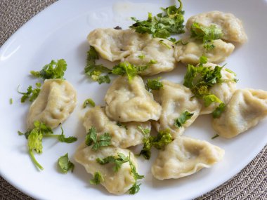 İnce doğranmış kişniş yapraklı buğulanmış hamur köfteleri beyaz bir tabakta servis edilir ve bu iştah açıcı yemeğin yakın çekim görüntüsünü sunar.