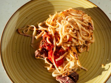 Lezzetli et ve zengin domates sosuyla tatlandırılmış, canlı sarı bir tabakta dinlenen ev yapımı makarna, her durum için mükemmel ve tatmin edici bir yemek sunar.