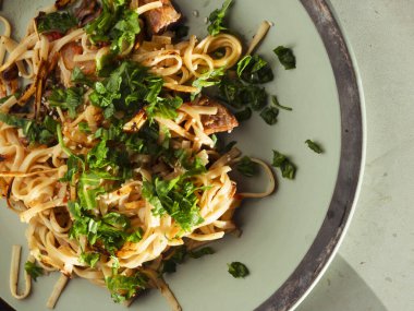 Et, susam tohumu ve yeşil bir tabakta dinlenen maydanozla tatlandırılmış nefis ev yapımı makarna görsel olarak çekici ve iştah açıcı bir mutfak deneyimi yaratıyor.