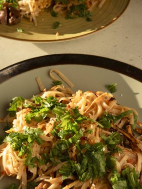 Taze otlar ve susam tohumlarıyla tatlandırılmış ev yapımı makarna tabakta servis edilir, güneş ışığıyla yıkanır, sıcak ve davetkar bir mutfak sahnesi yaratır.