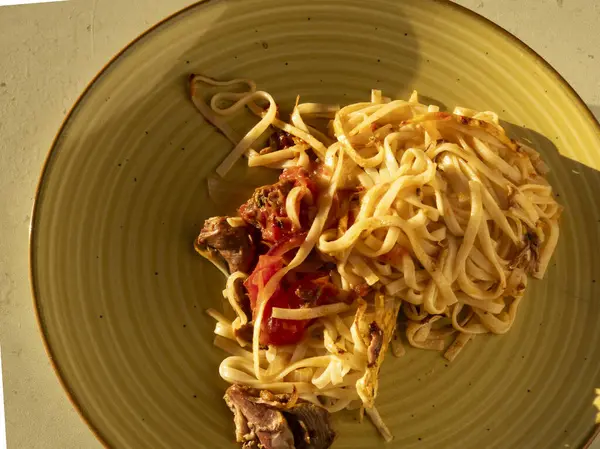 Lezzetli ev yapımı makarna, lezzetli et ve zengin domates sosuyla tatlandırılmış, canlı sarı bir tabakta sunulmuş, sıcak ve davetkar bir mutfak deneyimi yaratıyor.