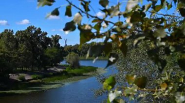 Kyiv 'deki Rusanivka Halk Parkı' nın sakin sularında dimdik duran Ukrayna Anıtı 'nı yeşil ağaçlar çerçeveletir.