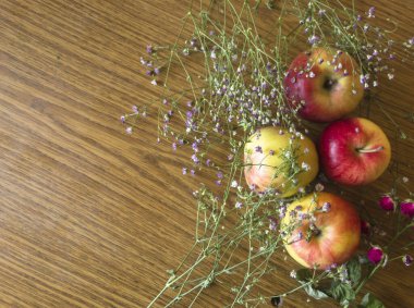 Taze toplanmış elmalar ve çingene çiçekleri, sonbahar bolluğu ve doğal güzelliği çağrıştıran, rustik ahşap bir masa üzerinde büyüleyici bir hayat kompozisyonu oluşturur.