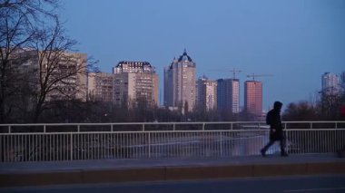 Scenic view from a moving train window revealing a modern city skyline with skyscrapers and a bridge over a river at twilight, capturing the essence of urban commuting and evening city life