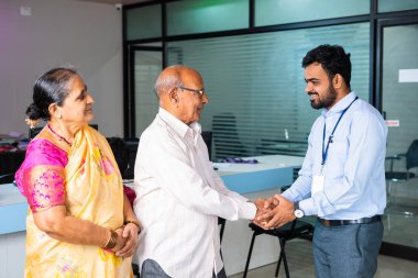 Bankadaki yaşlı çiftin elini sıkarak mutlu gülümseyen bankacı selamlaması - finansal destek kavramı, bankacılık danışmanı ve danışma