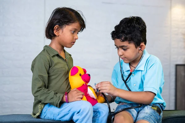 Young kids playing with stethoscope checking heartbeat of teddy bear at home - concept of future doctor, childhood lifestyles and togetherness.