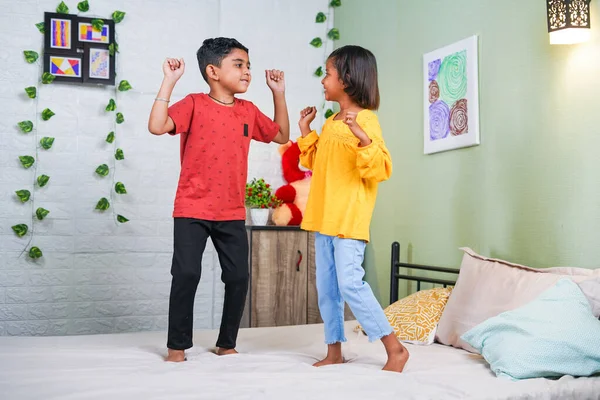 Happy smiling sibling kids dancing by jumping on bed at home - concept of playful childhood, bonding and relationship