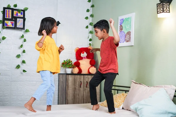 Happy smiling sibling kids dancing by jumping on bed at home - concept of playful childhood, bonding and relationship