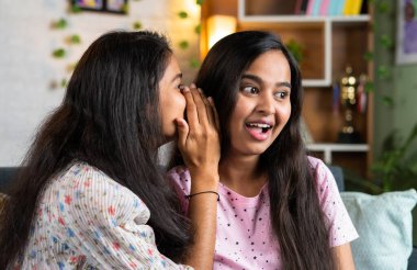 young teenager girl sharing secrets to sisterat home - concept of whispering, communication and trust