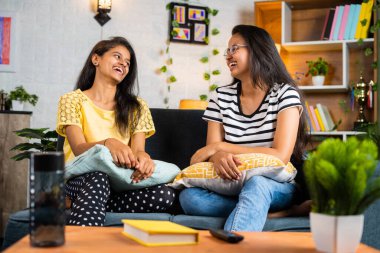 Happy smiling sibling women having chat with talking each other while sitting on sofa at home - concept of communication, togetherness and relaxation.
