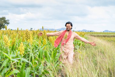 Happy smiling young farmer walking at corn field by feeling nature at framland - concept of happiness, freedom and carefree village lifestyle.