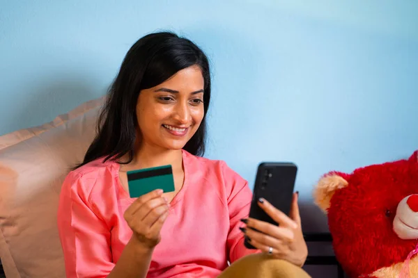 Happy young girl making online payment using credit card on mobile phone during sales or offers - concept of online secure transaction, shopping and e-commerce.