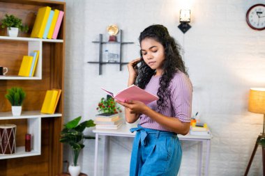 Serious young student reading book by walking around for examination at home - concept of dedication, learning and knowledge.