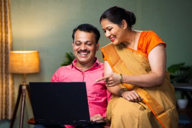 Evde koltukta otururken dizüstü bilgisayardan fırlayan mutlu ve mutlu bir çift. İlişki bağı, teknoloji ve online alışveriş kavramı..