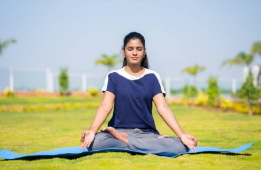 Yoga yapan ya da parkta gözleri kapalı meditasyon yapan genç bir kadın - rahatlama, kendine bakım ve sağlıklı yaşam tarzı kavramı.