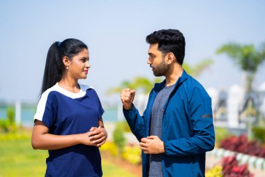 Ciddi genç Hintliler ayaklarına dokunarak egzersiz yapıyorlar parkta oturarak - spor konsepti, aktif yaşam tarzı ve sabah rutini.