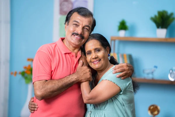 快乐的印度老年夫妇站在一起 互相拥抱 看着家里的相机 家庭关系 放松和退休生活方式的概念 — 图库照片