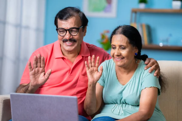 一对快乐的印度老年夫妇在家里沙发上一边用笔记本电脑一边谈论视频通话 在线交流 退休生活方式和网络空间的概念 — 图库照片