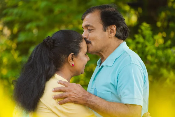 快乐的老年男人或丈夫在公园里拥抱妻子 亲吻他的额头 情感上的结合 身体上的亲密和浪漫的时刻 — 图库照片