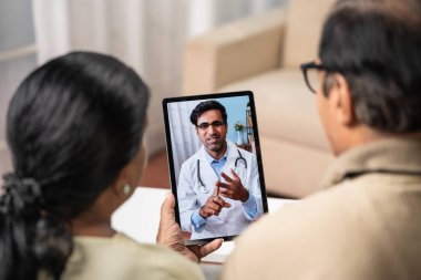 Hintli yaşlı çiftin evdeki internet üzerinden yapılan video görüşmeleri sırasında doktordan tavsiye alırken çekilmiş omuz fotoğrafı - uzaktan sağlık, sanal danışma ve e-sağlık konsepti.
