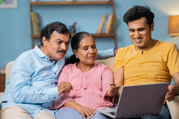 快乐的印度成年儿子 与年迈的父母坐在沙发上坐在笔记本电脑前聊天 财产选择 网上购物和家庭关系的概念 — 图库照片