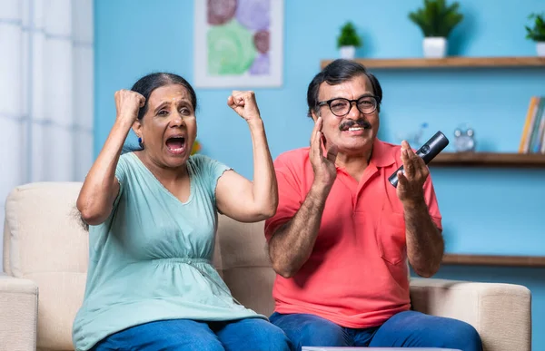 快乐而兴奋的印度老年夫妇坐在沙发上观看电视或电视直播板球比赛 娱乐的理念 老年人的支持和退休的生活方式 — 图库照片