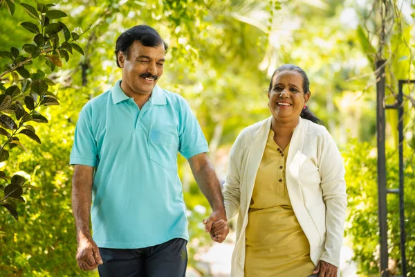 stock image indian senior couple walking by talking each other at park - concept of relationship, relaxation and retirement lifestyle.