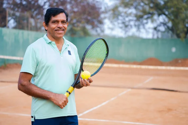 Щасливий Індійський Старший Чоловік Ракеткою Ячем Дивлячись Камеру Тенісному Корті — стокове фото