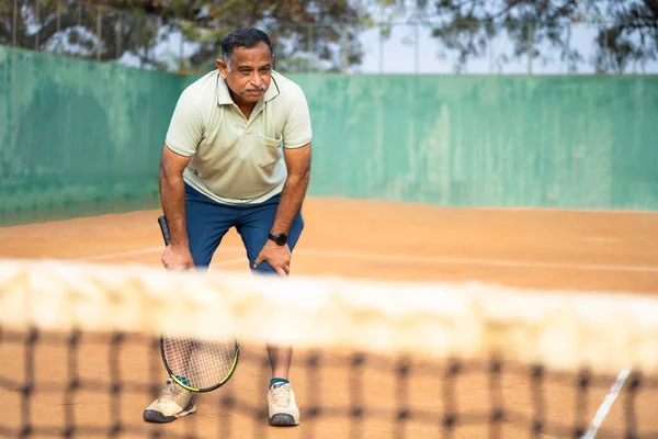 Indian tired exhausted senior tennis player breathing heavily after playing tennis match at court - concept of stamina, endurance and healthy lifestyle.