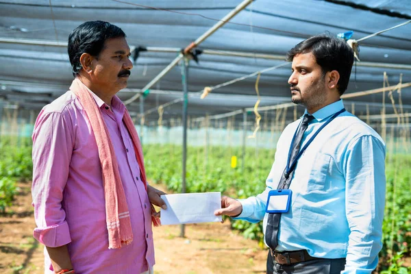 Indian bank officer giving notice to farmer at greenhouse - concept of debt, financial problems and loss in business