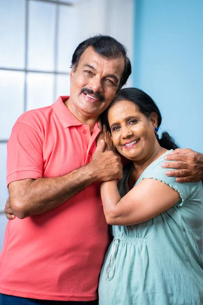 在家庭关系 放松和享受的概念下 印度一对快乐的老年夫妇站在一起 一边相互拥抱一边看着镜头 一边看着自己的家 这是一张垂直的照片 — 图库照片